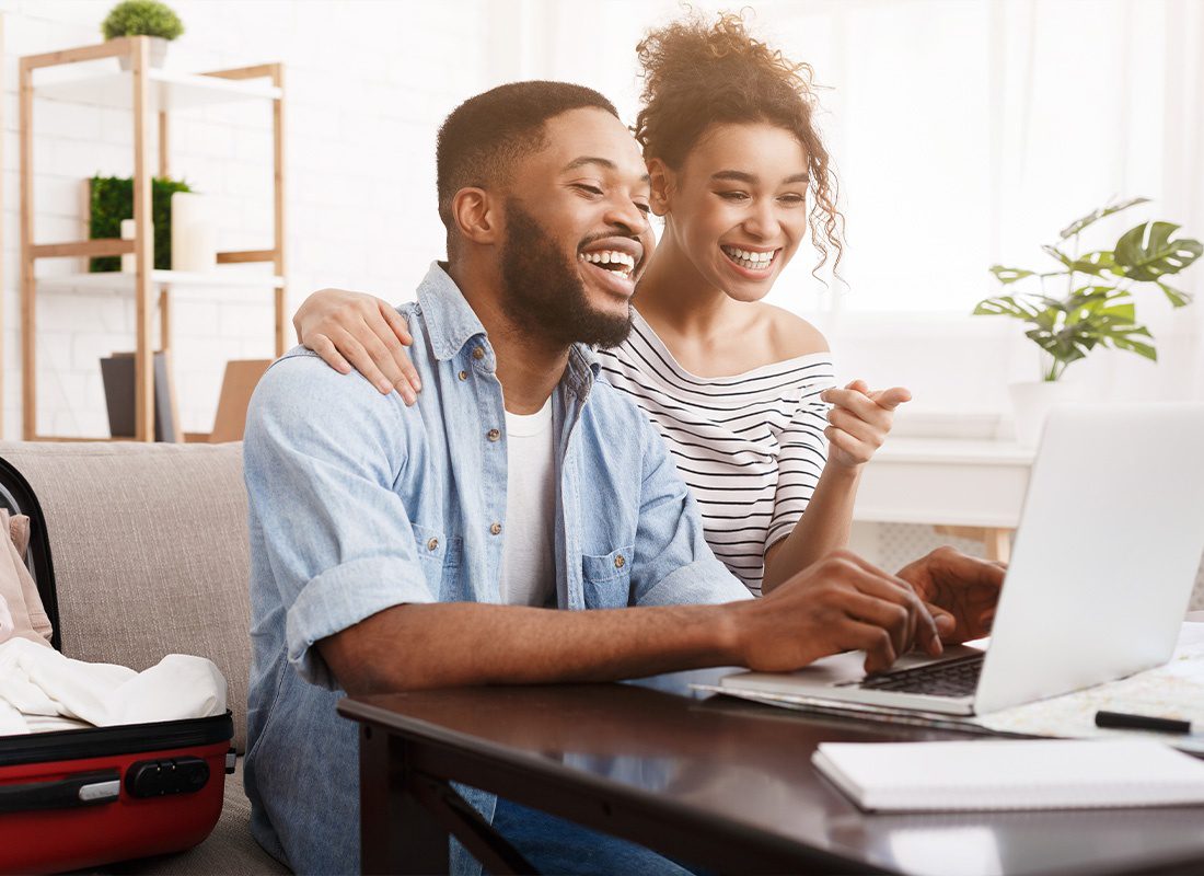 Insurance Solutions - A Couple Smiling and Pointing at a Laptop Resting on a Wooden Table While Sitting on Their Living Room Couch
